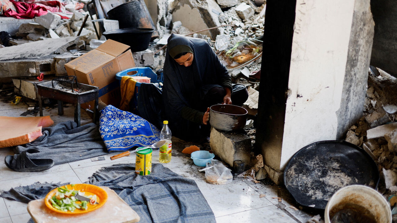 FILE PHOTO: A Palestinian woman cooks, with the rubble of residential buildings destroyed during the war visible in the background, in Jabalia, northern Gaza Strip, January 6, 2026. REUTERS/Mahmoud Issa/File Photo