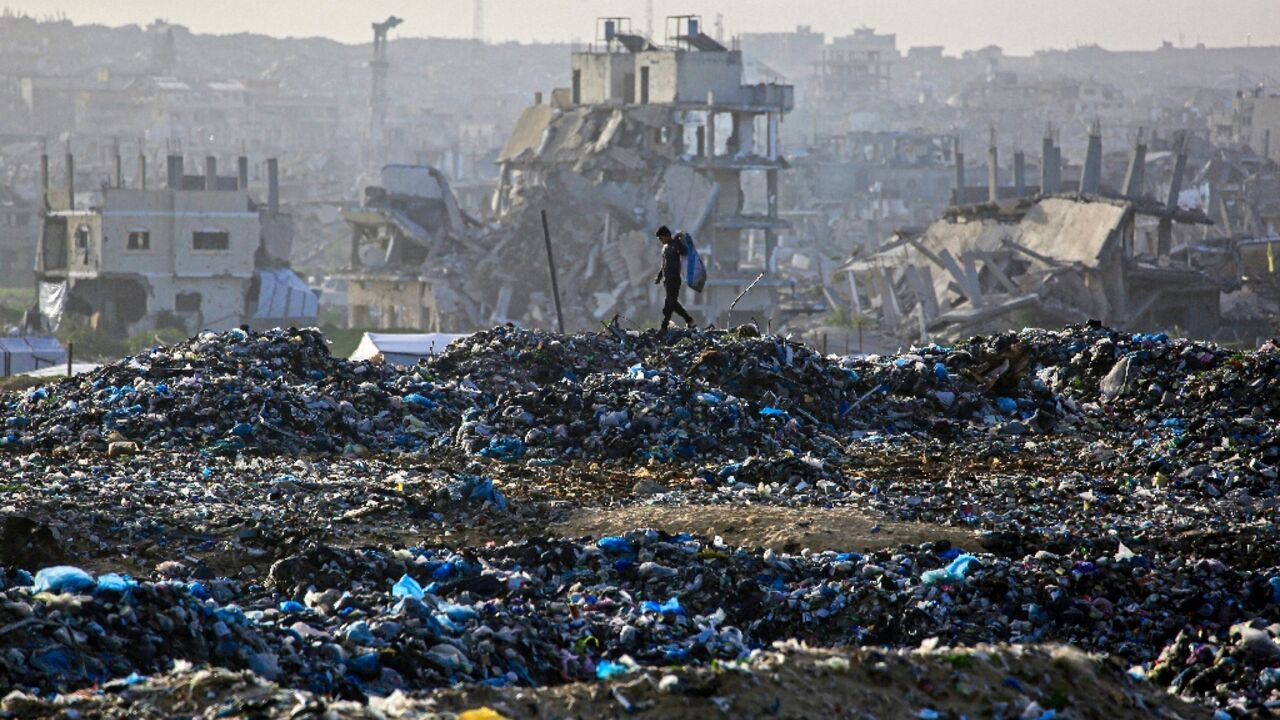 A Palestinian boy searches for recyclable material at a landfill against the backdrop of destroyed buildings in Khan Yunis, in the southern Gaza Strip on January 25, 2026. Since October 10, a fragile US-sponsored truce in Gaza has largely halted the fighting between Israeli forces and Hamas, but both sides have alleged frequent violations.