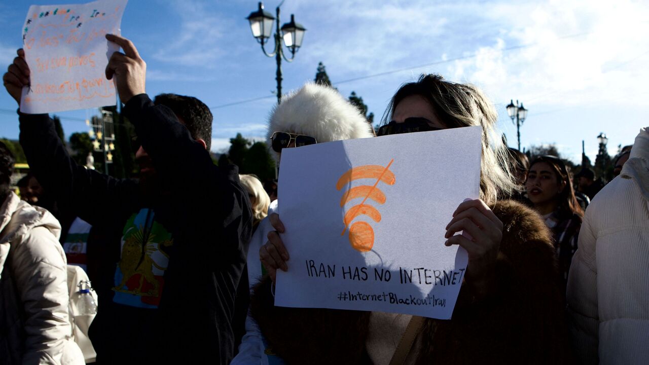 Backlit image of Iranian demonstrators holding national flags and portraits during an antiKhamenei protest at Syntagma Square in Athens, Greece, on January 11, 2026. What stands out is a woman holding a placard featuring a Wi Fi symbol and the message "Iran has no internet," referencing an internet blackout in Iran. The gathering takes place in front of the Hellenic Parliament, where protesters primarily supporters of the former Shah express opposition to the current Iranian regime and denounce restrictions