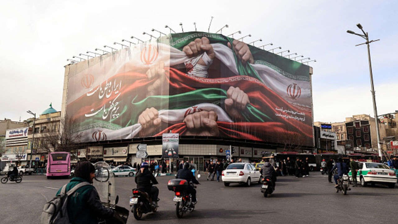 Vehicles pass by a large patriotic banner depicting the Iranian flag on Enghelab Square in Tehran on January 14, 2026. (ATTA KENARE / AFP via Getty Images