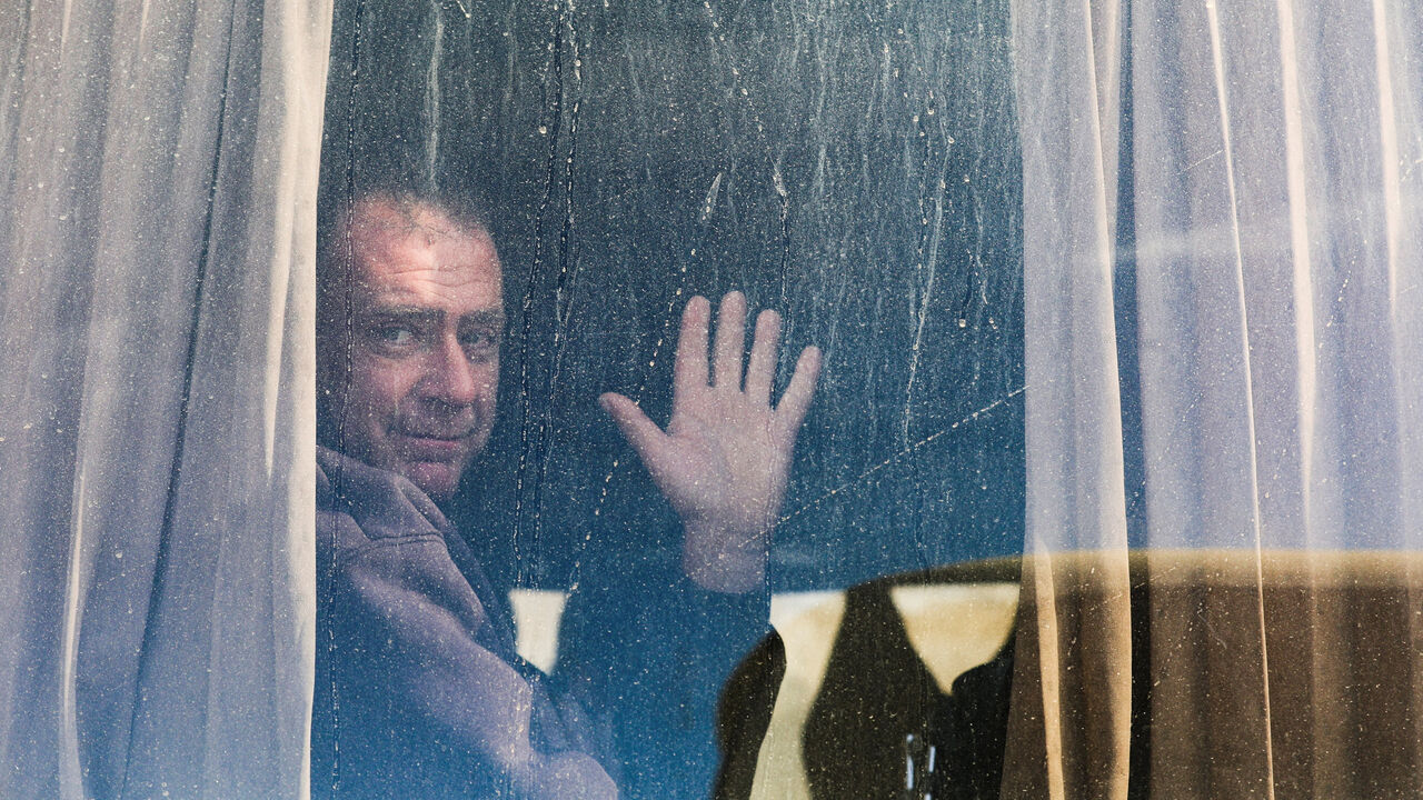 A Palestinian man waves from a window as war-wounded people and patients, accompanied by relatives, get ready to leave Gaza for treatment abroad through the Rafah border crossing between Gaza and Egypt, after it was opened by Israel on Monday for a limited number of people, in Khan Younis in the southern Gaza Strip, February 3, 2026. REUTERS/Ramadan Abed