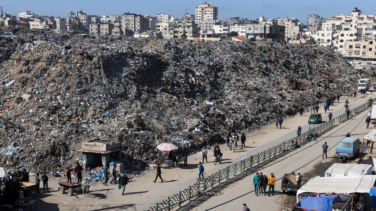 People walk past a large mound of rubbish at a landfill site surrounded by residential buildings in Gaza City, February 11, 2026. REUTERS/Dawoud Abu Alkas