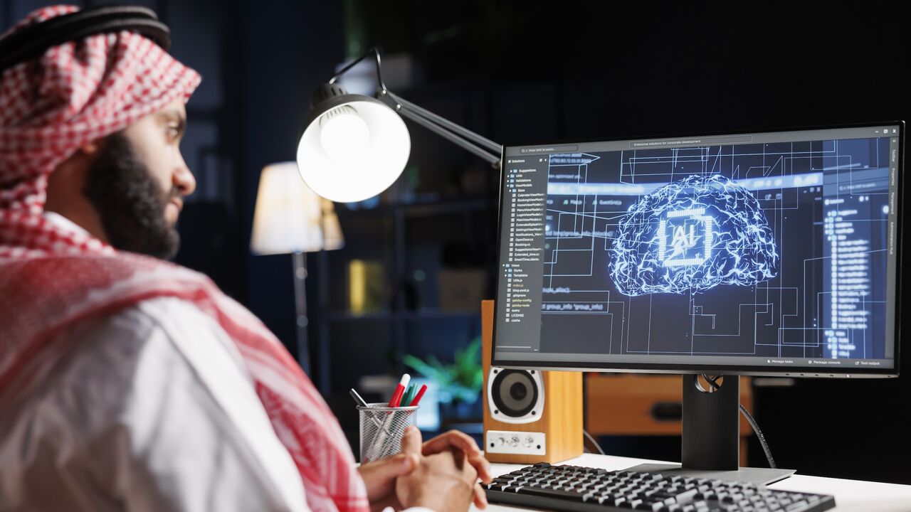 Detailed image of Middle Eastern developer in front of desktop pc monitoring a complex network, ensuring data security and efficient computing using cloud, AI and machine learning.