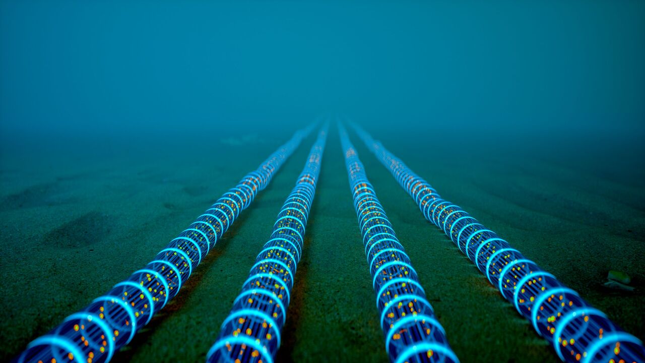 High-tech fiber optic cables glowing with blue light extend into the distance on the ocean floor — Getty Images Stock Photo