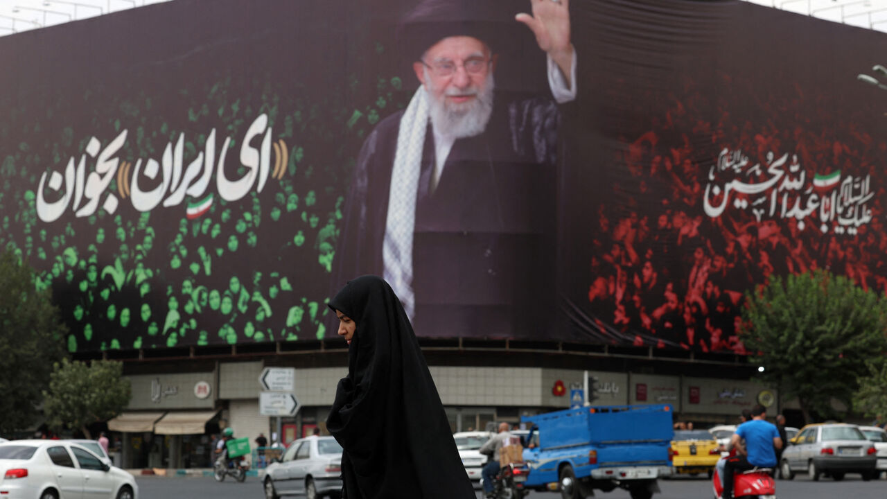 TOPSHOT - An Iranian crosses a street next to a billboard bearing the portrait of Iranian supreme leader Ayatollah Ali Khamenei and a quote reads in Persian 'Sing Oh Iran' at the Enqelab Square in Tehran on July, 9, 2025. (Photo by AFP) (Photo by -/AFP via Getty Images)