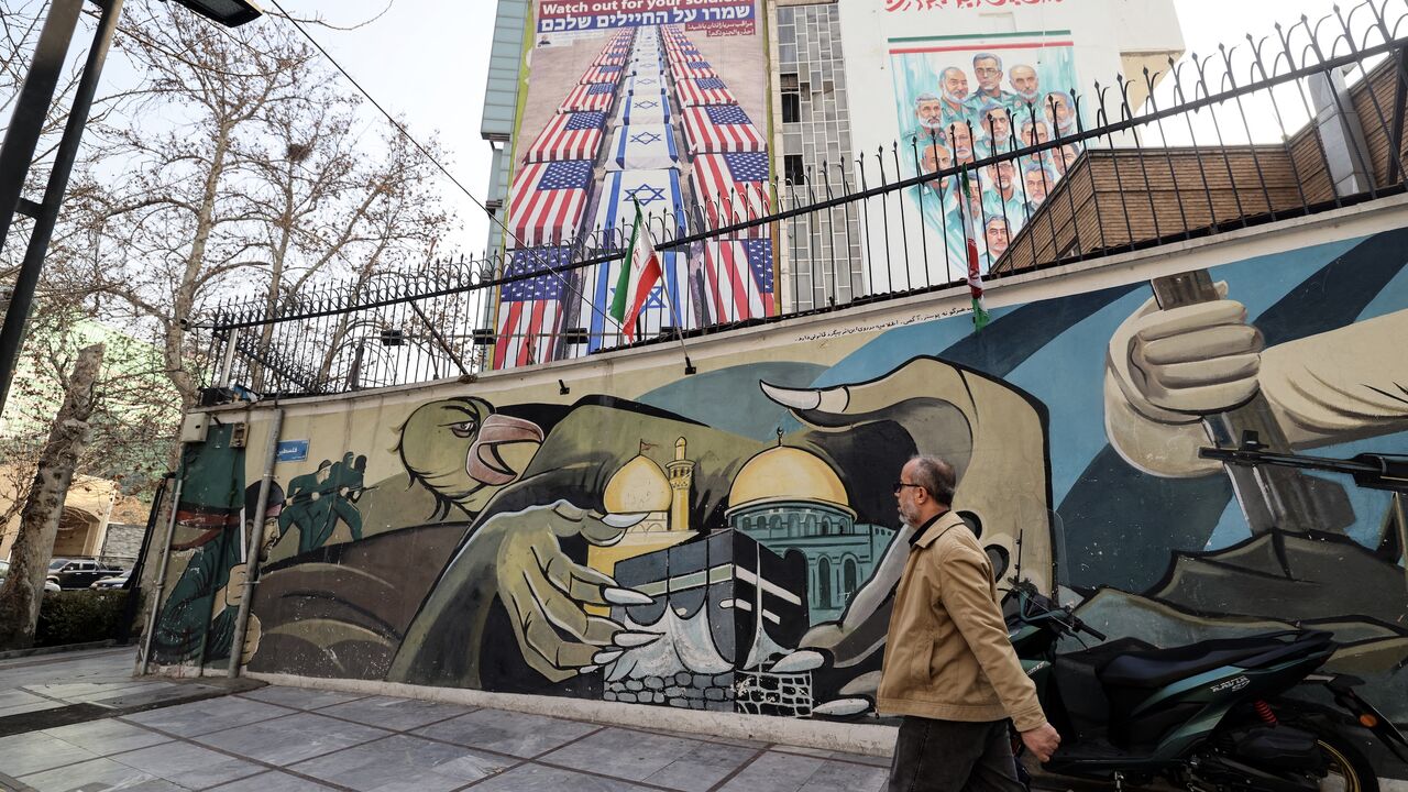An Iranian man walks past an anti-US and anti-Israel banner hanging on a building in Palestine Square in Tehran on Jan. 27, 2026.