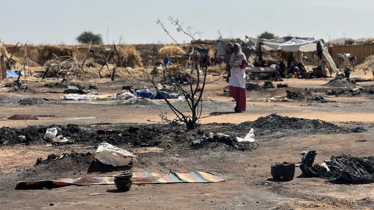 A displaced Sudanese woman who left El-Fasher after its fall with others, walks amid the remains of a fire that broke out at a camp in Tawila on Feb. 11, 2026. 