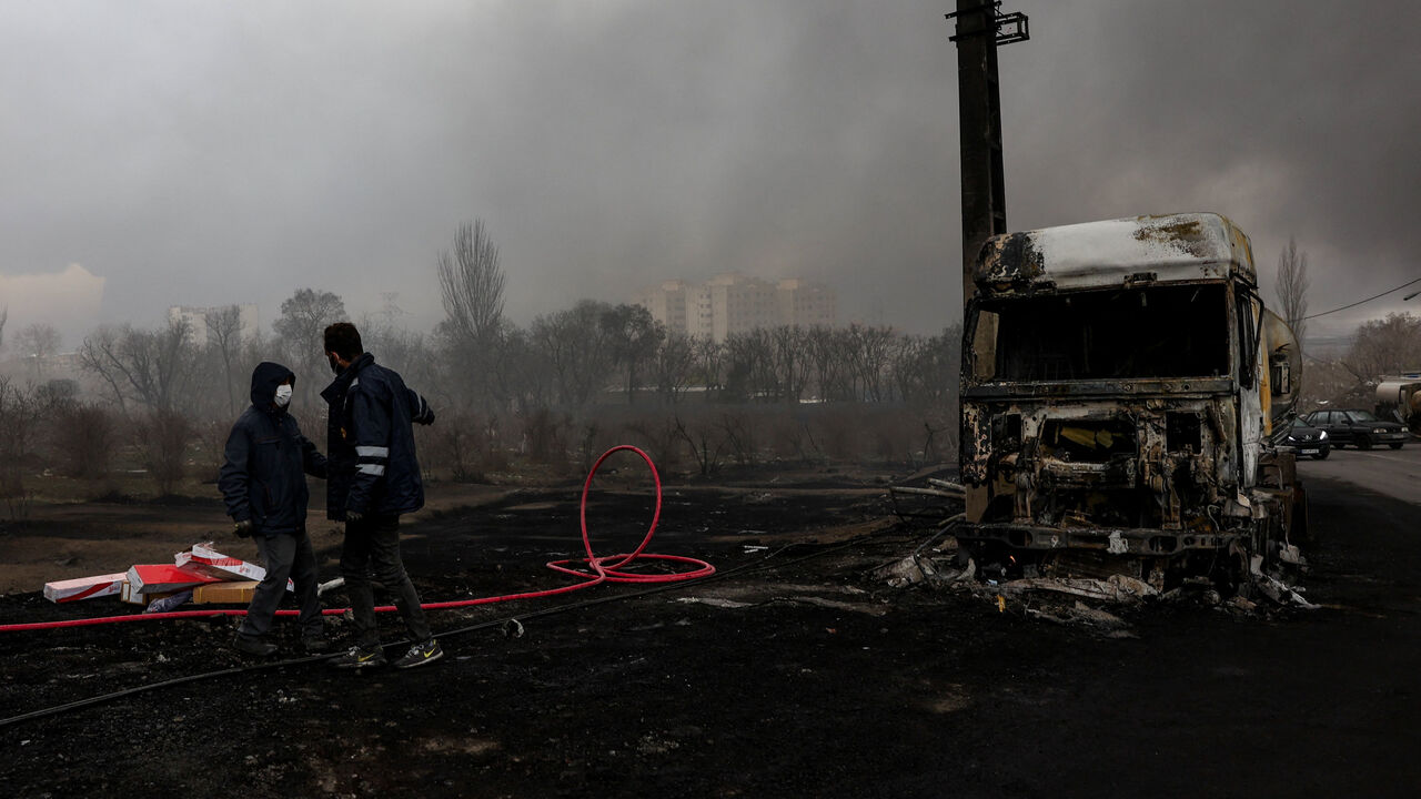 People stand near a destroyed vehicle as smoke rises after a reported strike on Shahran fuel tanks, amid the U.S.-Israeli conflict with Iran, in Tehran, Iran, March 8, 2026. Majid Asgaripour/WANA (West Asia News Agency) via REUTERS