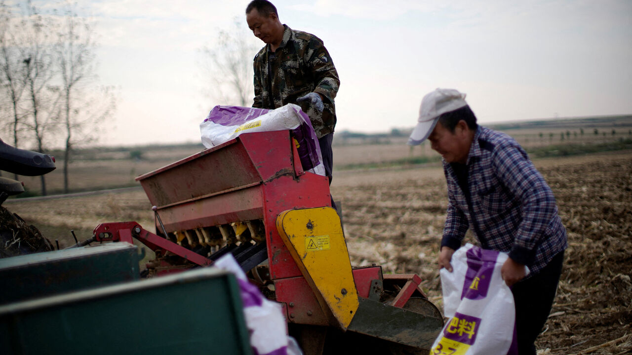 FILE PHOTO: Farmers load sacks of fertiliser into a seeder on a wheat field in Nanyang, Henan province, China October 13, 2021. REUTERS/Aly Song/File Photo