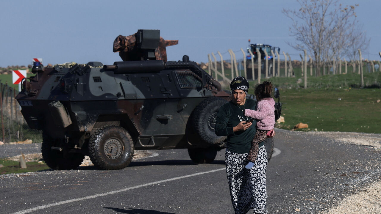 A woman carrying a child walks past an armoured vehicle as Turkish army and security personnel search a field after a piece of ammunition fell following the interception of a missile launched from Iran by a NATO air defence system, in Diyarbakir, Turkey, March 9, 2026. REUTERS/Sertac Kayar