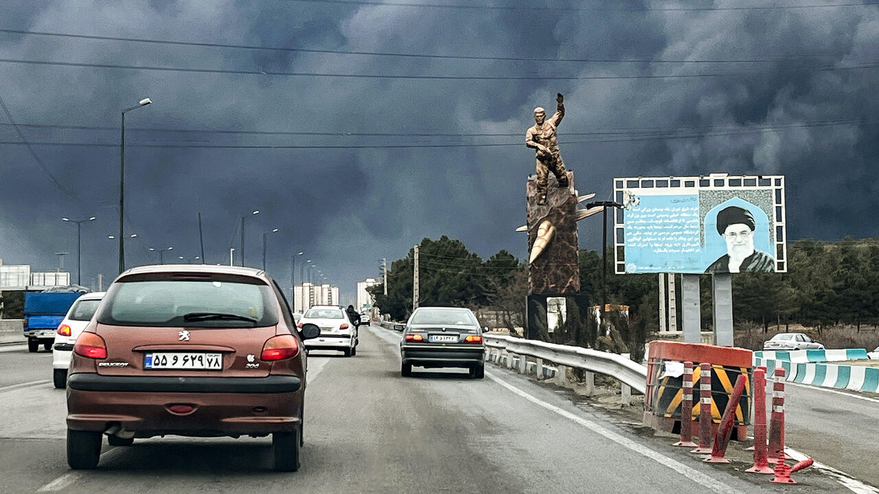 Vehicles move along a highway past a war memorial statue and a billboard depicting Iran's late supreme leader Ayatollah Ali Khamenei who was killed in an air strike on Feb. 28, with plumes of black smoke billowing, in Tehran on March 8, 2026. 