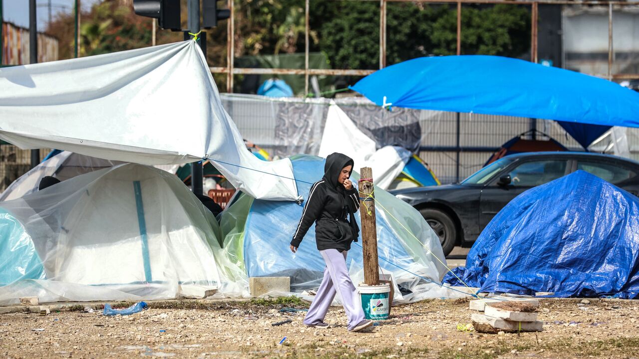 A displaced girl walks past tents covered in plastic sheeting to shield them from the stormy weather along Beirut's seafront area on March 15, 2026. 