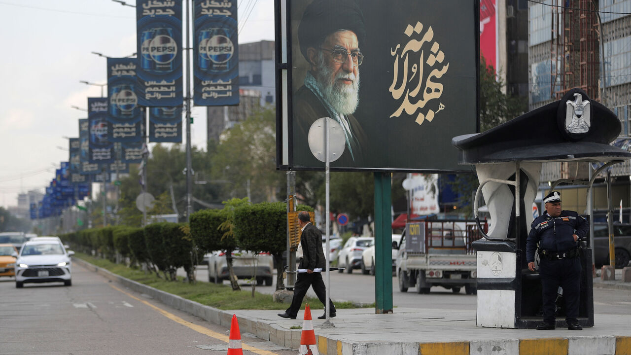 An Iraqi police officer stands guard as a man walks beneath a billboard bearing a portrait of Iran's slain supreme leader Ayatollah Ali Khamenei in Baghdad on March 25, 2026. Iraq will submit a formal complaint to the United Nations Security Council over strikes in its territory, the office of the prime minister said on March 25, following an attack in the country's west that killed seven security personnel. Iraq has been drawn into the Middle East war triggered by the US-Israel attack on its neighbour Iran