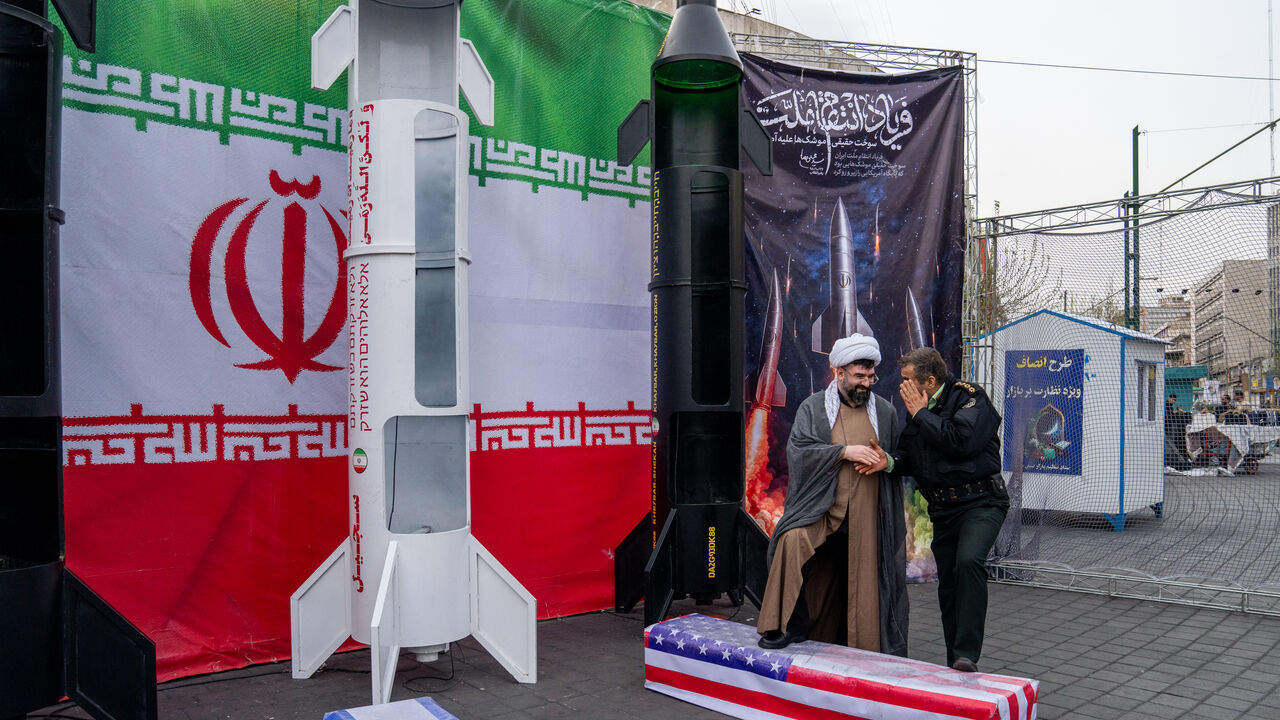Two people stand near mock missiles and caskets displaying the Israeli and U.S. flags during a demonstration in support of the Iranian government on March 22, 2026 in central Tehran, Iran. (Photo by Majid Saeedi/Getty Images)
