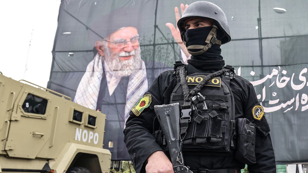 A member of the Iranian security forces stands guard next to a banner honoring Iran's slain supreme leader, Ayatollah Ali Khamenei, in Tehran on March 31, 2026. 