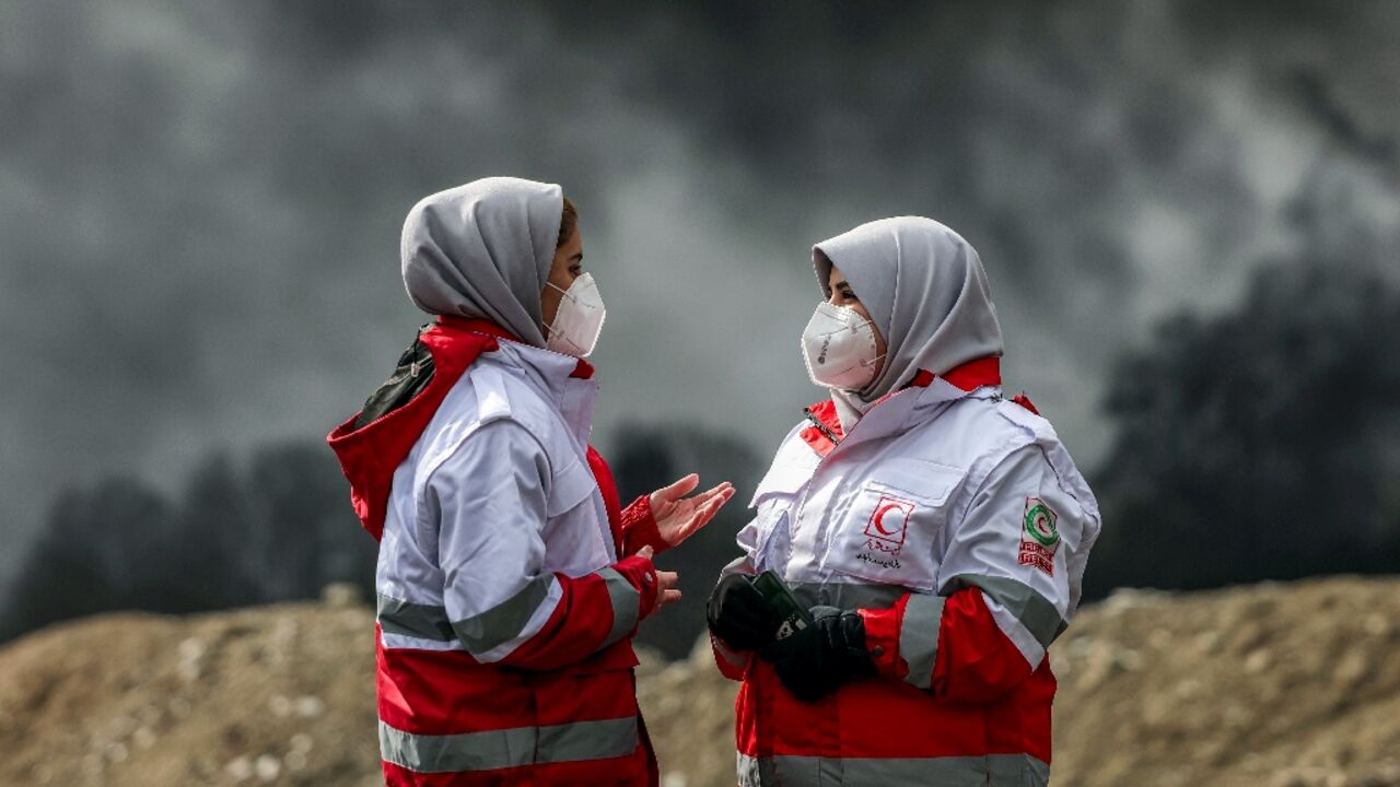 Members of Iranian Red Crescent Society standing near smoke plumes. The IFRC launched an emergency appeal to help support the IRCS's crisis response