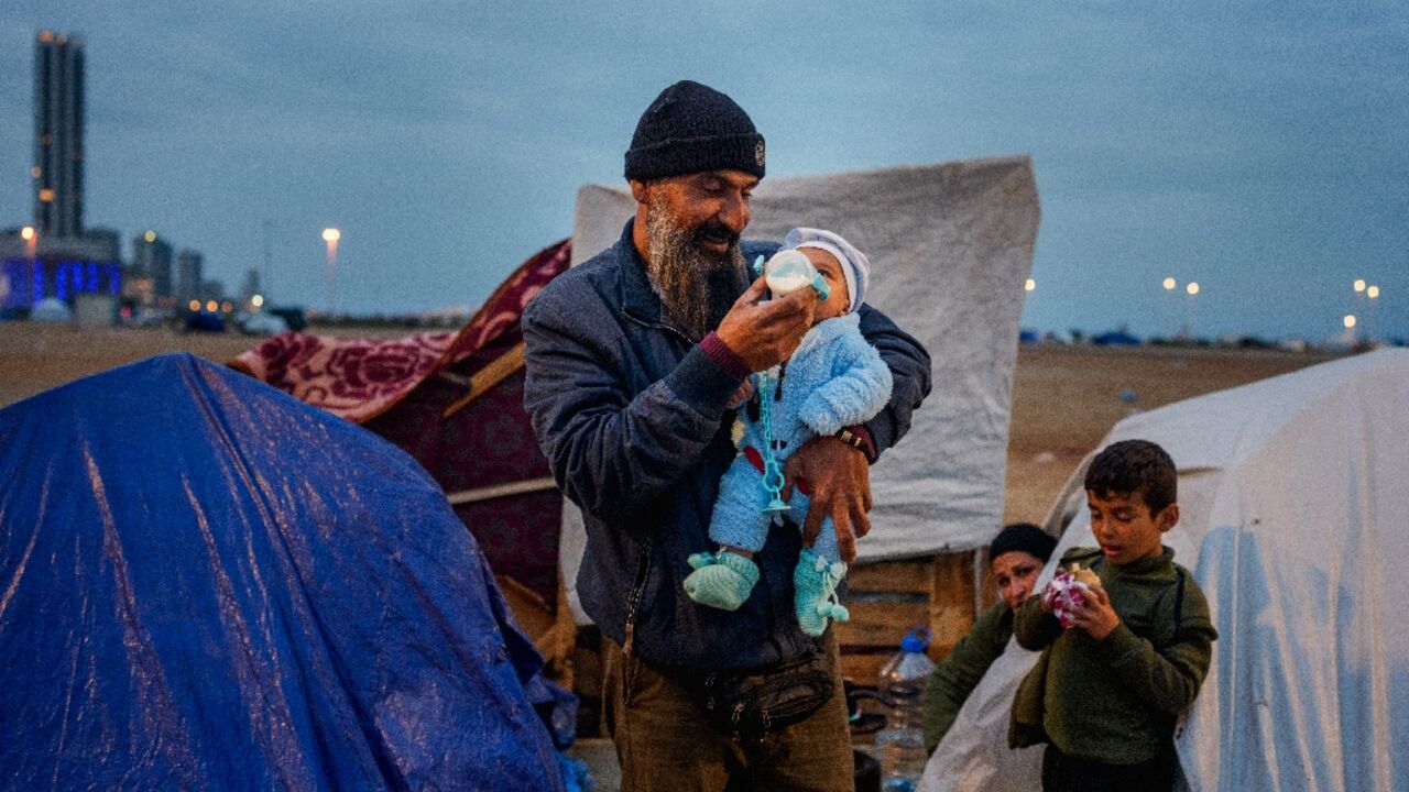 A man feeds his baby with a bottle at a make-shift camp for the displaced set up along the seafront in the Lebanese capital Beirut