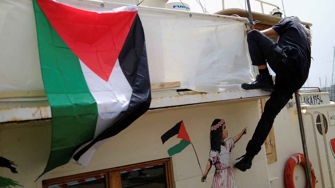 A Palestinian flag on a boat next to a member of a humanitarian flotilla preparing to depart for Gaza, in Barcelona, Spain, April 11, 2026. REUTERS/Nacho Doce,