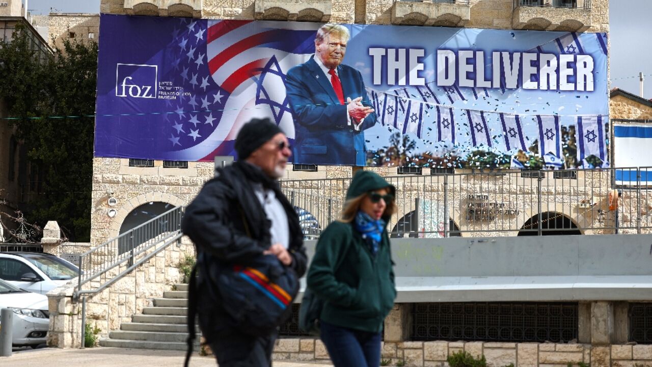 People walk past a banner in Jerusalem depicting US President Donald Trump with the slogan 'The Deliverer' in Jerusalem 