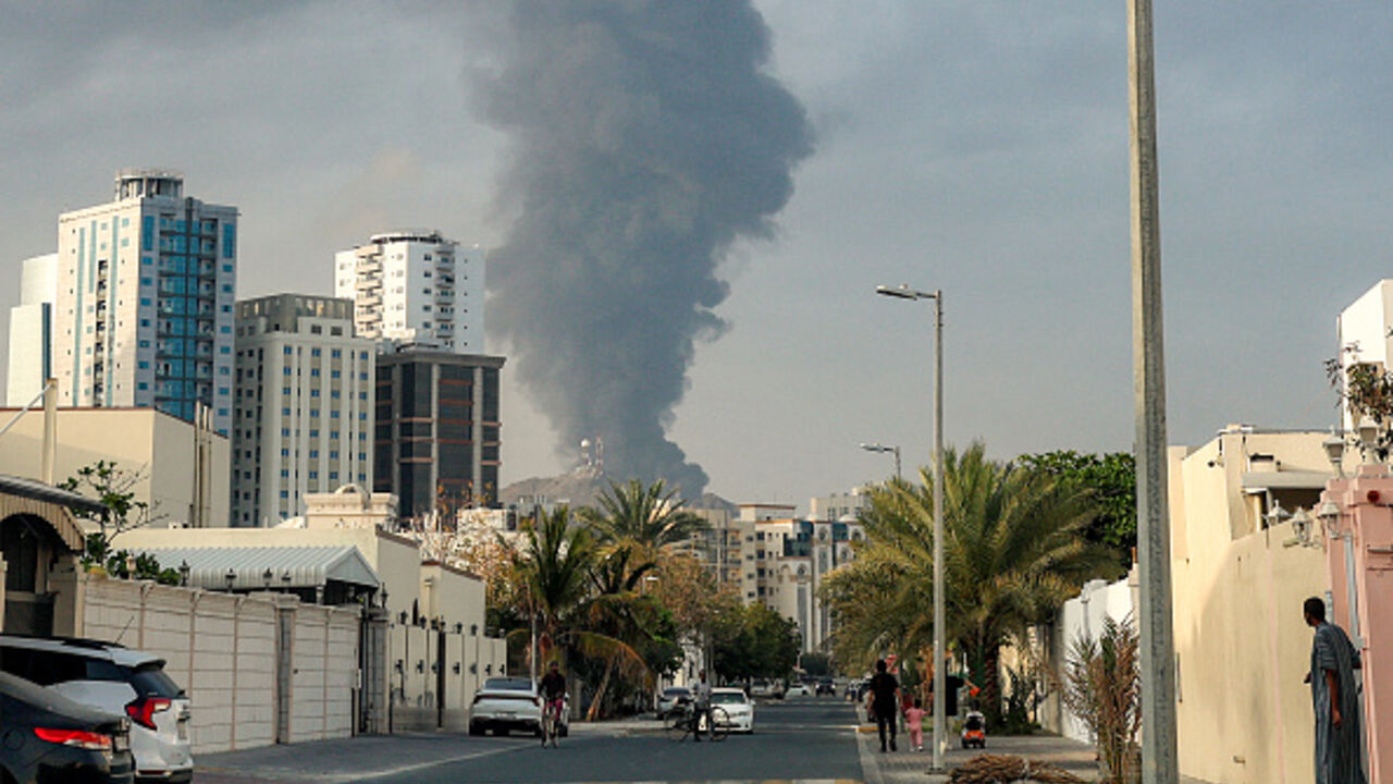 TOPSHOT - People watch from a street as a tall smoke plume billows following an explosion in the Fujairah industrial zone on March 3, 2026. Iran's strikes on Gulf neighbours since February 28, following the US-Israeli attack, forced the UAE to shut its airspace, blindsiding travellers who thought they were headed to one of the region's safest holiday destinations. (Photo by Fadel SENNA / AFP via Getty Images)