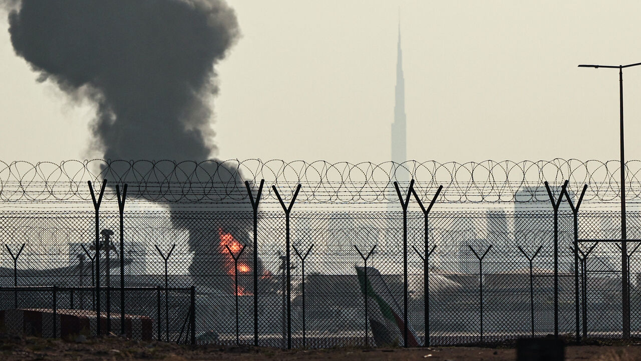 The Dubai skyline with the landmark Burj Khalifa skyscraper (R) is pictured as a smoke plume rises from an ongoing fire near Dubai International Airport on March 16, 2026. Flights were gradually resuming at Dubai airport on March 16, previously the world's busiest for international flights, the airport operator said, after a "drone-related incident" sparked a fuel tank fire nearby, as Iran kept up its Gulf attacks. (Photo by AFP via Getty Images) /