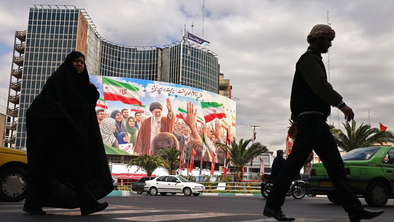 Commuters make their way past a giant billboard of slain Iranian supreme leader Ayatollah Ali Khamenei at Valiasr Square in Tehran on April 19, 2026. 
