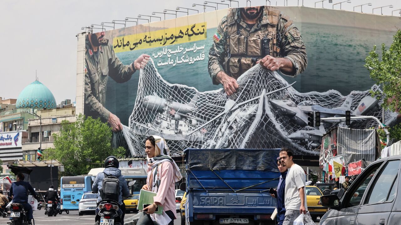 Iranian walks past a giant billboard reading "The Strait of Hormuz remains closed" at the Revolution Square in Tehran on April 22, 2026.