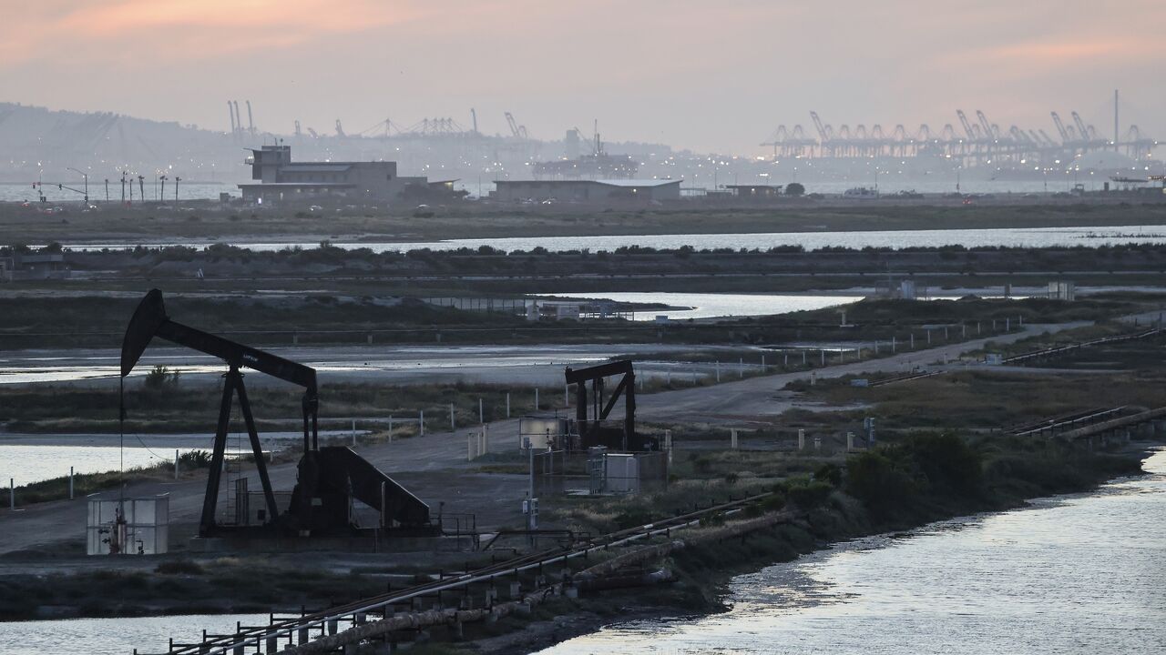 A pumpjack stands idle in the Huntington Beach oil field, with port cranes visible in the distance, on April 23, 2026, in Huntington Beach, California.