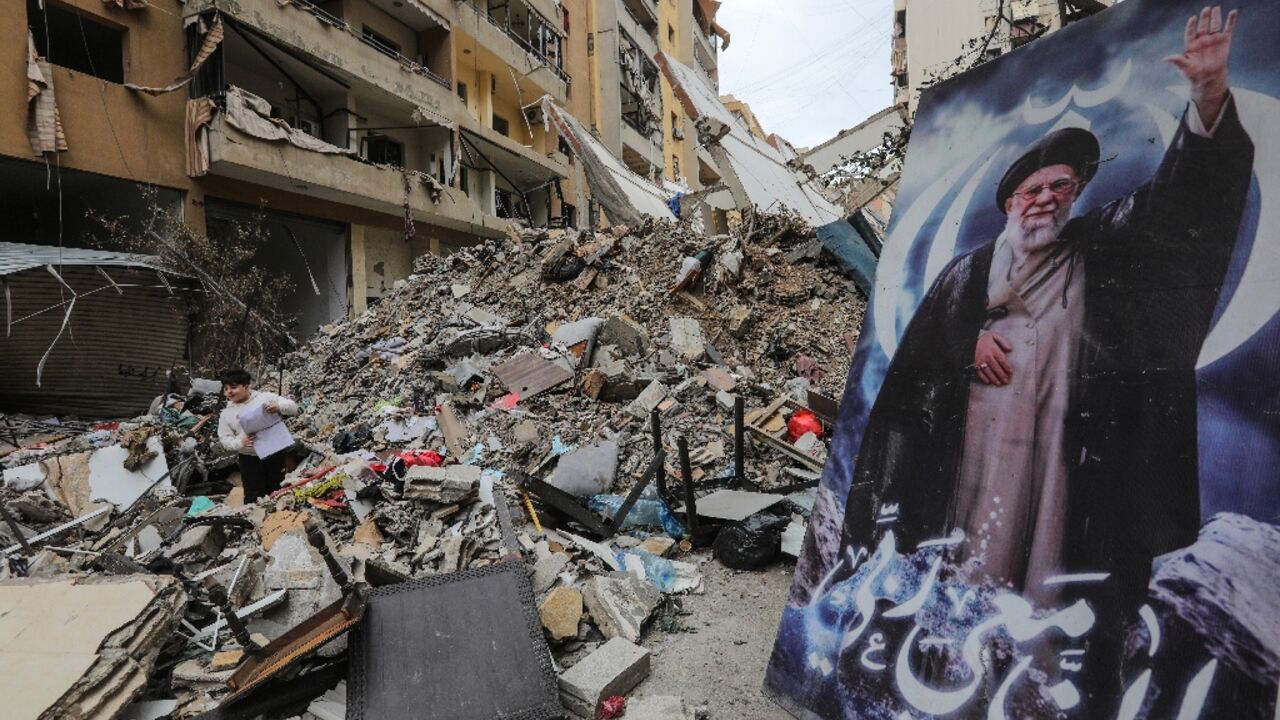 A boy stands amid the debris of a destroyed building next to a portrait of Iran's slain supreme leader Ayatollah Ali Khamenei 