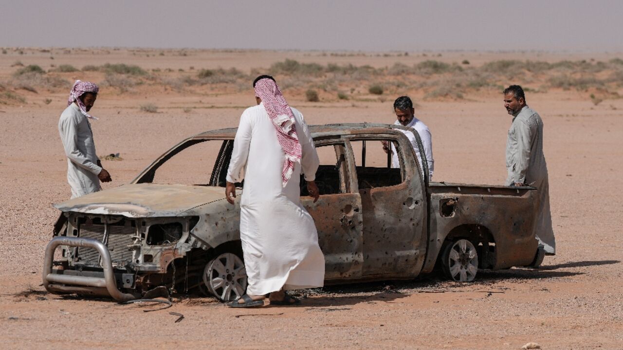 Men gather around the husk of a destroyed pickup truck in southwestern Iraq