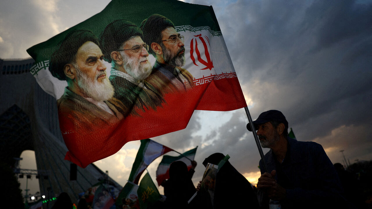 FILE PHOTO: A man holds a flag with a picture of late leader of the Islamic Revolution Ayatollah Ruhollah Khomeini, late Supreme Leader of Iran Ayatollah Ali Khamenei and Iran's new Supreme Leader Mojtaba Khamenei, during a rally in Tehran, Iran, April 29, 2026. Majid Asgaripour/WANA (West Asia News Agency) via REUTERS/File Photo
