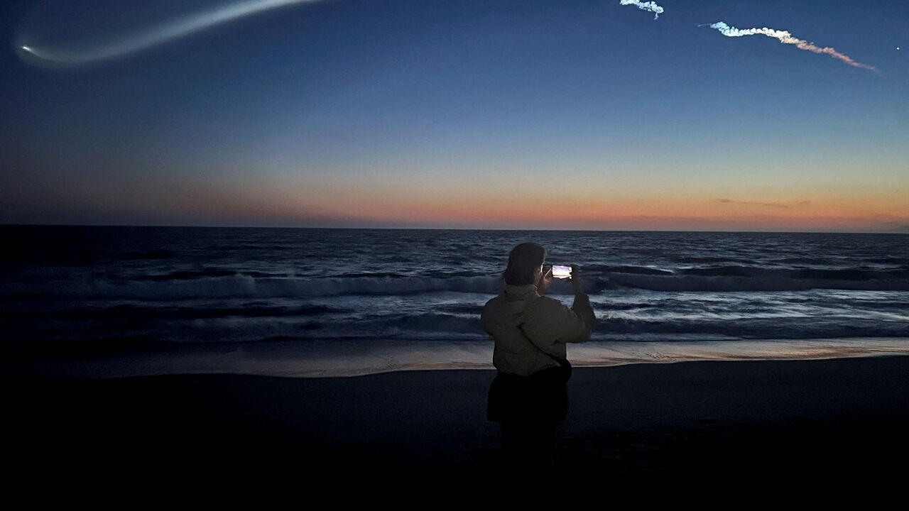 FILE PHOTO: A person takes photos of a trail as the Falcon 9 carrying Starlink satellites streaks across the sky in the latest SpaceX launch as viewed from Venice Beach in Los Angeles, California, U.S., April 6, 2026.   REUTERS/Daina Beth Solomon/File Photo