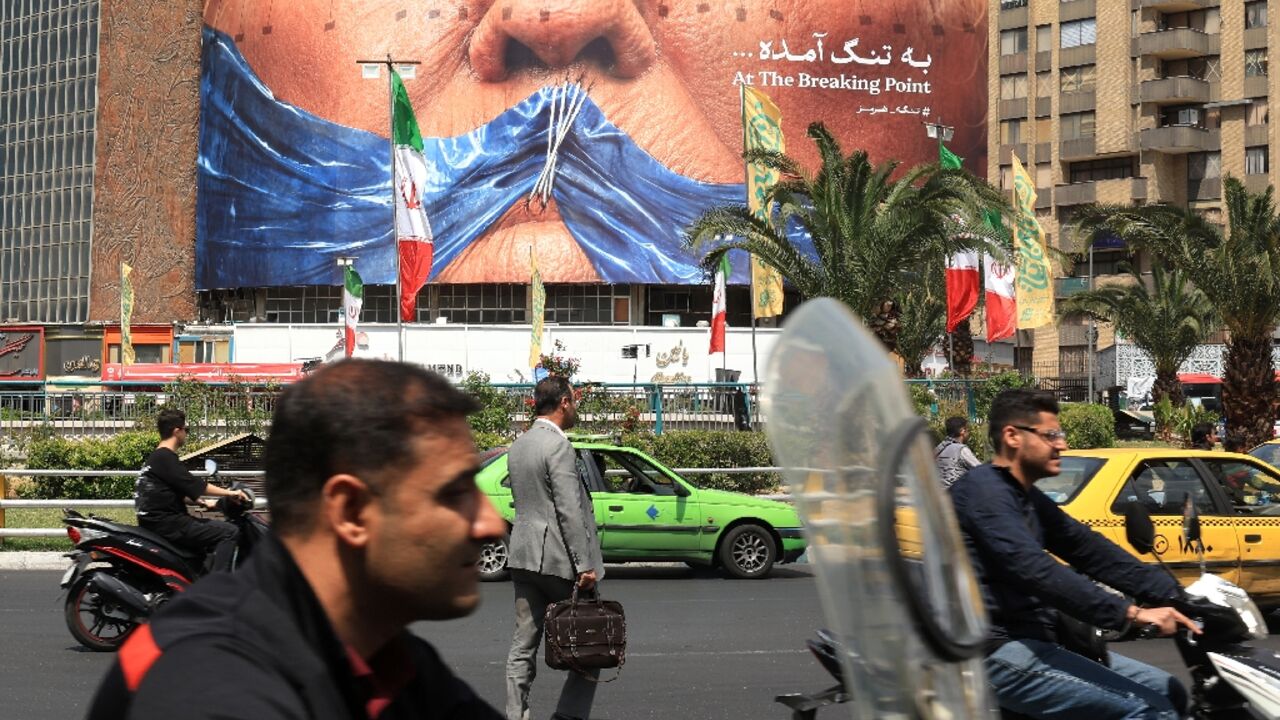 Commuters make their way past an anti-US billboard referring to President Donald Trump and the Strait of Hormuz, installed on a building at the Valiasr Square in Tehran