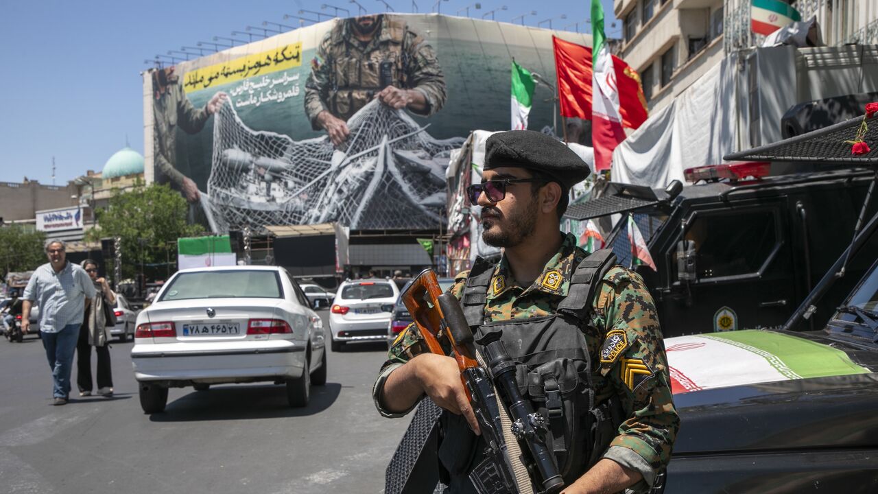 An Iranian police office stands on patrol near a poster depicting Iranian soldiers holding a net in the shape of the Strait of Hormuz, with US military aircraft ensnared in a fishing net, on May 9, 2026 in Tehran, Iran. 