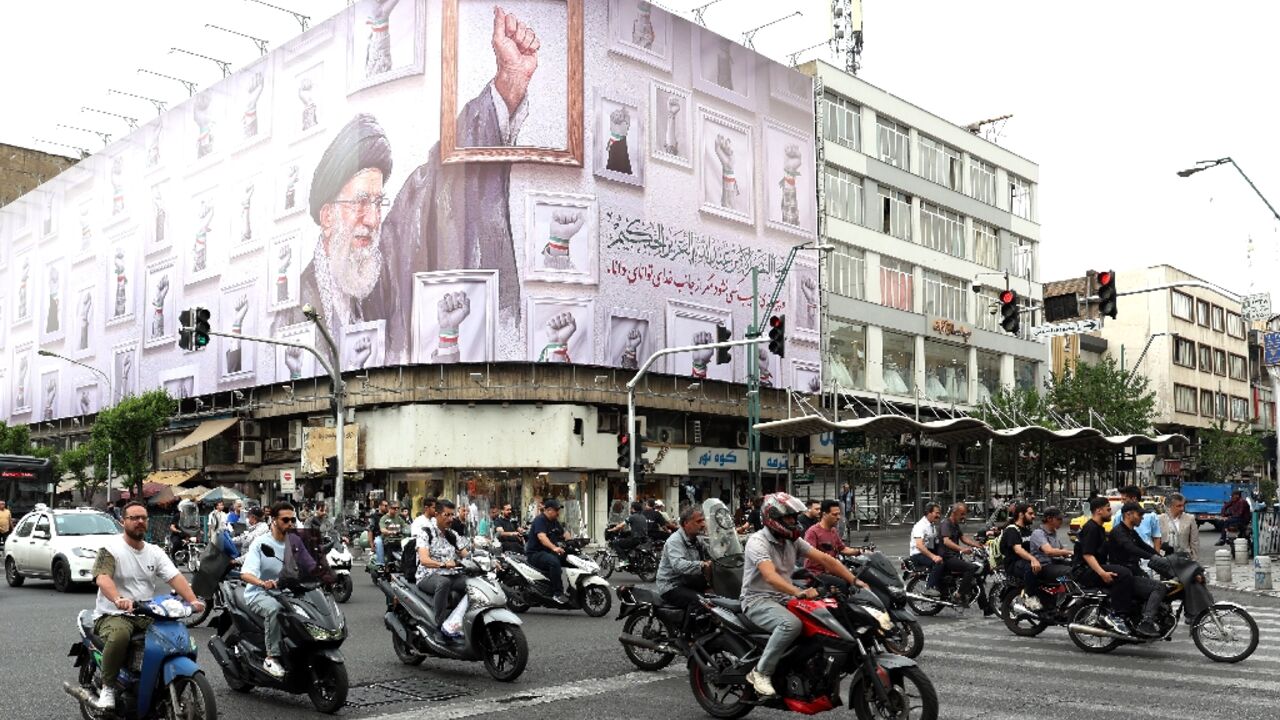 Iranians drive past a billboard in Tehran with the image of late supreme leader Ayatollah Ali Khamenei, killed in the US-Israeli strikes that started the war in February