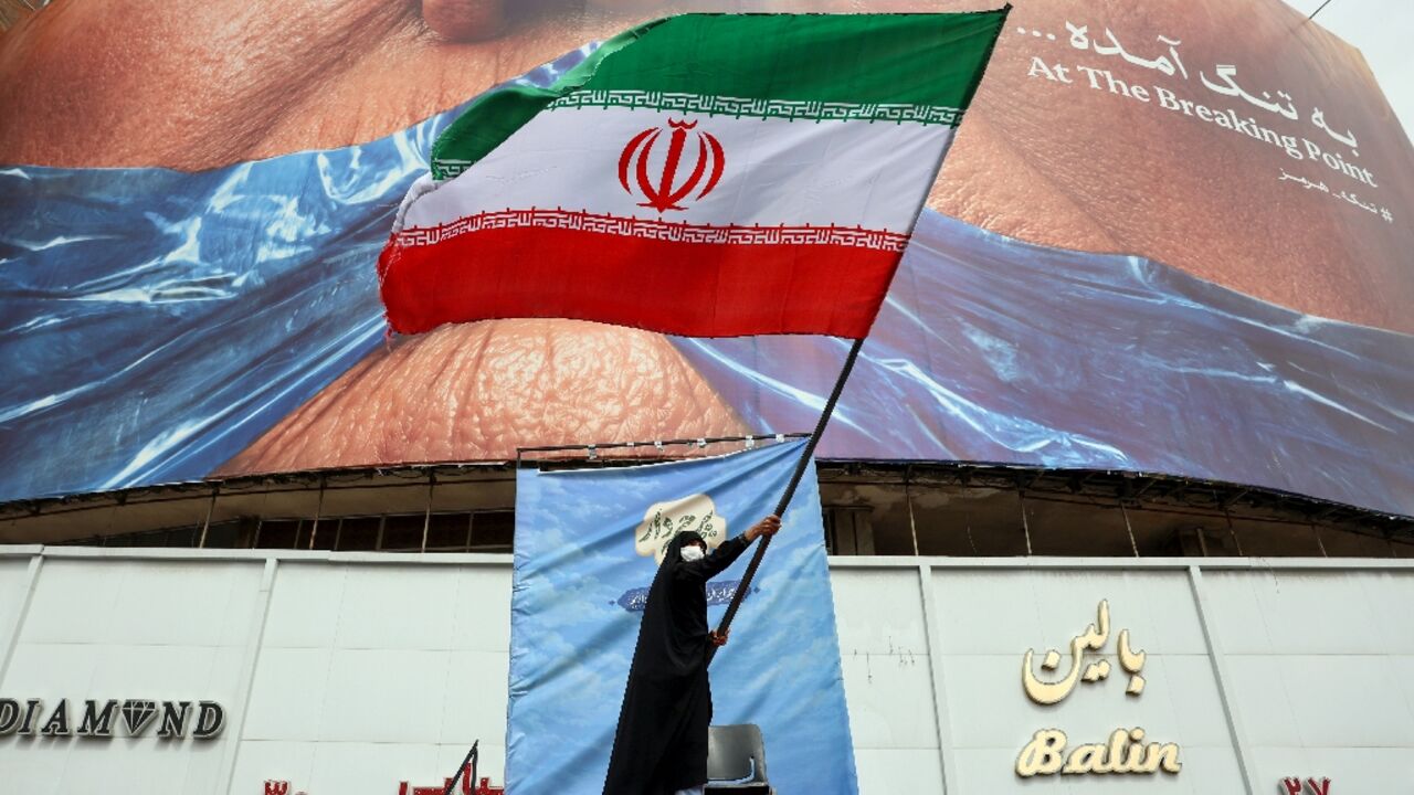 A woman waves an Iranian flag in front of an anti-US billboard referring at Valiasr Square in Tehran
