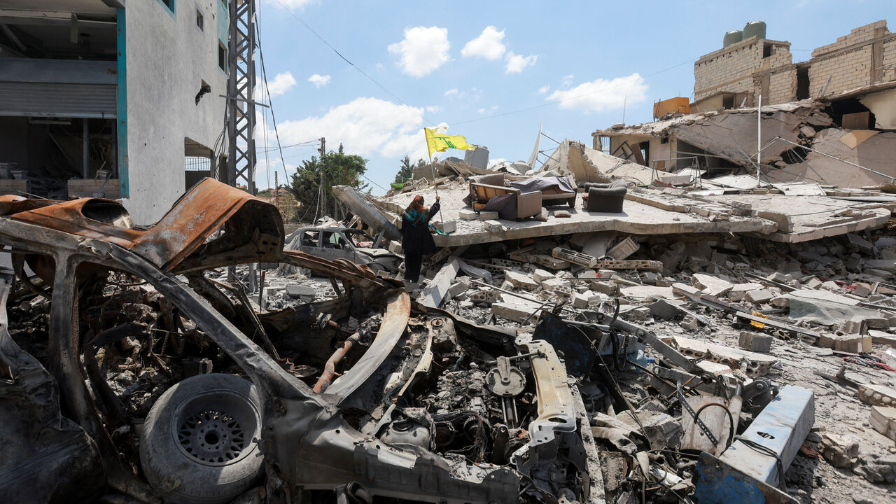 A woman holds a Hezbollah flag amid rubble of destroyed buildings, in Deir Qanoun al-Nahr, Tyre district, southern Lebanon,  June 15, 2026. REUTERS/Aziz Taher