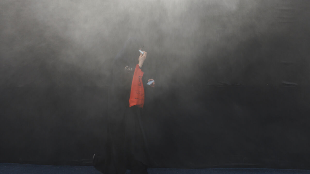 A Shi'ite Muslim woman walks through water mist sprayed to cool people from the heat ahead of Ashura, the holiest day on the Shi'ite Muslim calendar, in Karbala, Iraq June 25, 2026. REUTERS/Ahmed Saad