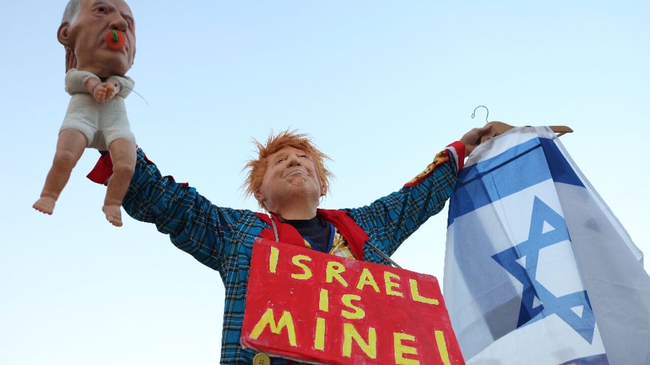 An Israeli left-wing activist in costume with a mask depicting US President Donald Trump holds a baby puppet depicting Israel's Prime Minister Benjamin Netanyahu during a demonstration against the government and the war in the Middle East