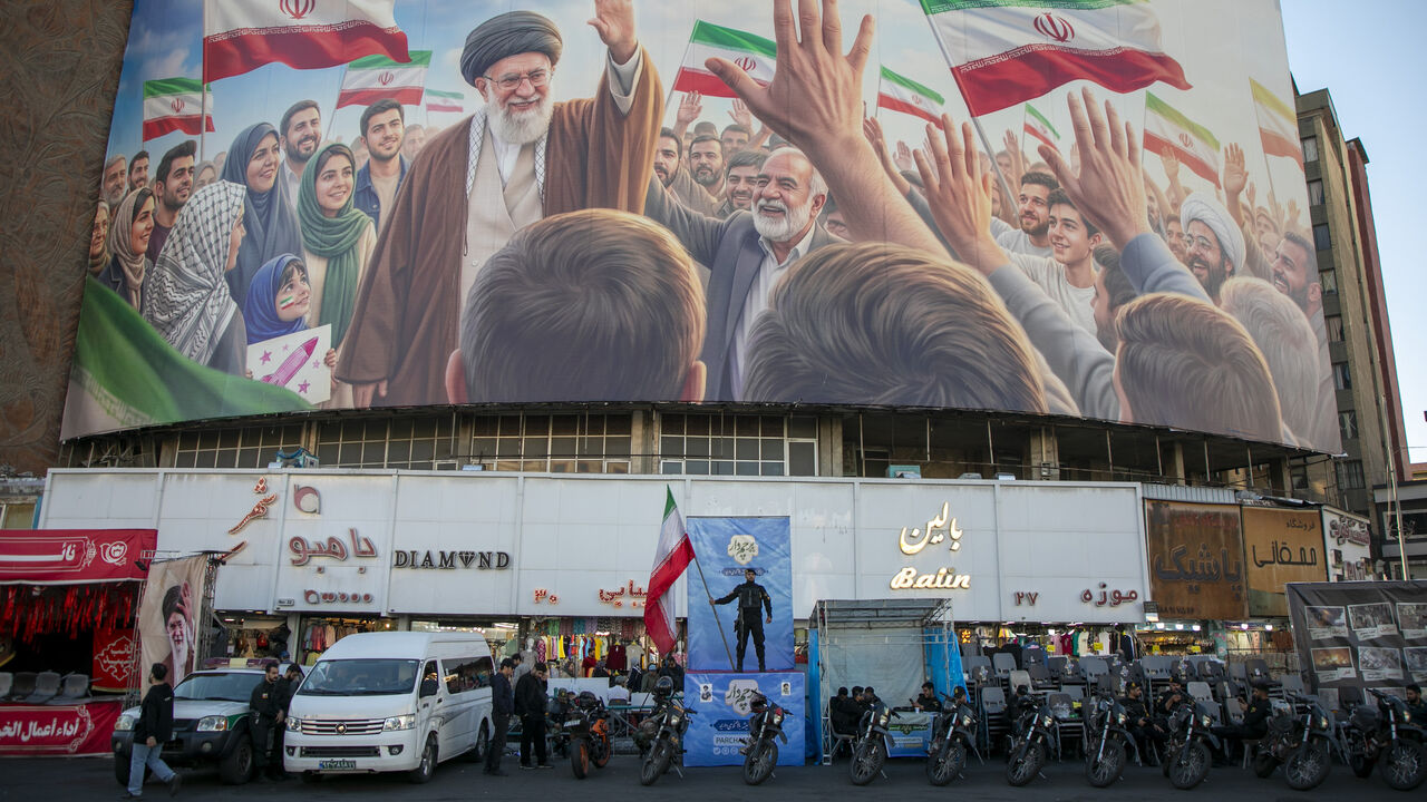 A police officer stands holding a flag in Valiasr Square beneath a mural of the late Ayatollah Ali Khamenei on April 23, 2026 in Tehran, Iran. 