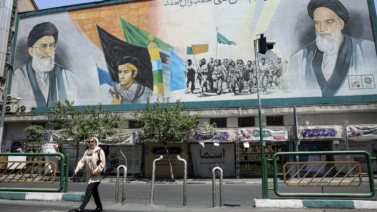 An Iranian woman walks past a mural depicting late Iranian supreme leaders Ayatollah Ali Khamenei (L) and Ayatollah Ruhollah Khomeini (R) in Tehran on June 18, 2026. 