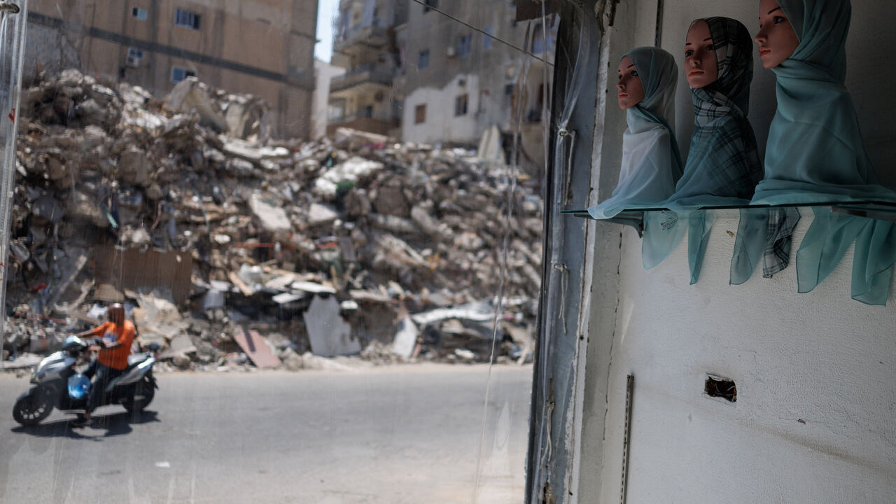 A motorcycle drives past as mannequin heads are displayed inside a reopened clothing store with blast-damaged windows, as rubble from a building destroyed in an Israeli strike is seen across the street, in Tyre, southern Lebanon, July 5, 2026. REUTERS/Zohra Bensemra