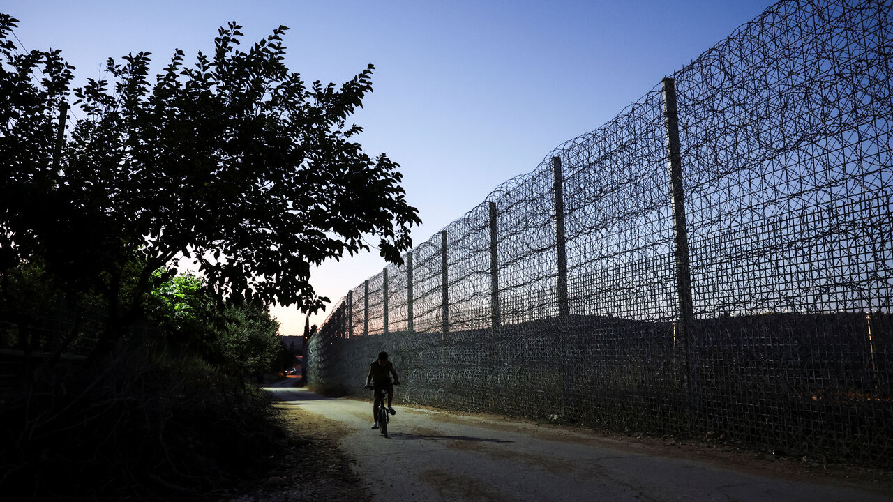 Yousef Foqahaa cycles past the tall metal fencing installed by the Israeli military that closed off four of the five entrances to his town, Sinjil, near Ramallah, in the Israeli-occupied West Bank, June 26, 2026. REUTERS/Ammar Awad