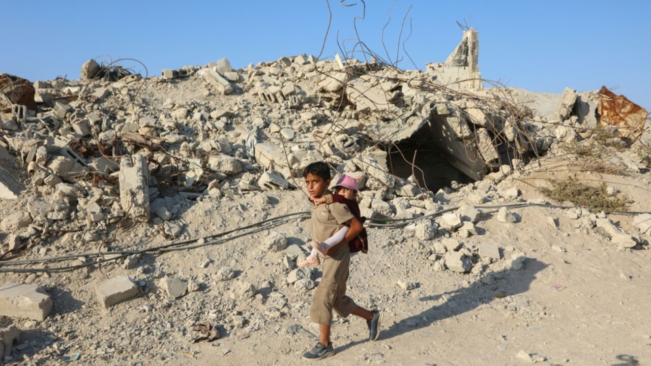 A Palestinian child carries a little girl on his back as he walks past the rubble of destroyed buildings in the Jabalia camp for Palestinian refugees in the northern Gaza Strip