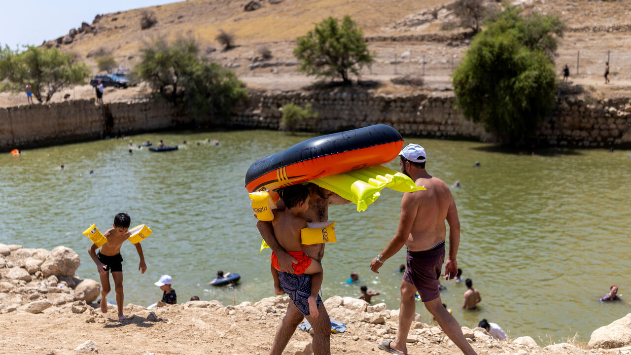 A man carries inflatables and a child as Israelis soak in an ancient water reservoir in the Jordan Valley in the Israeli-occupied West Bank, August 5, 2026. REUTERS/Ronen Zvulun