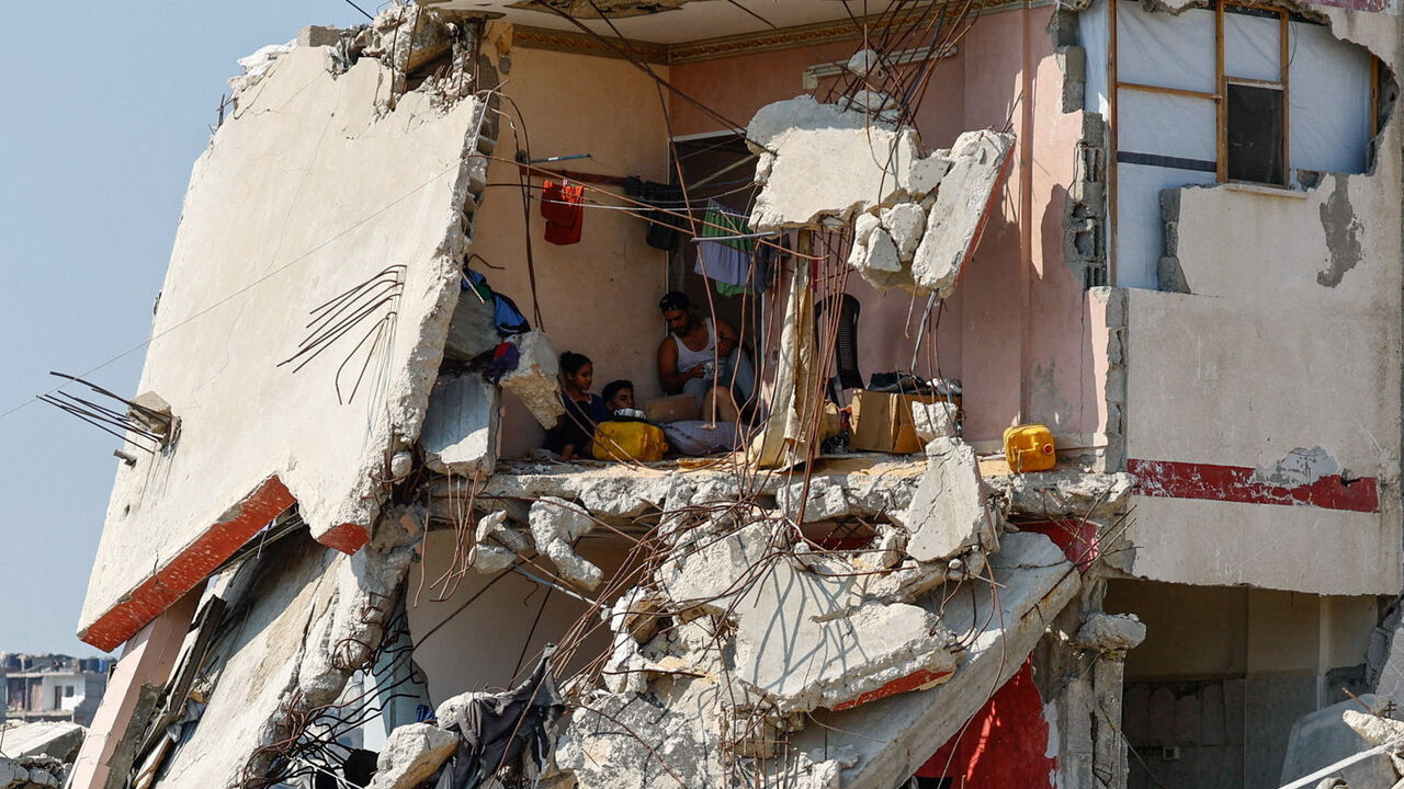 Palestinians sit inside a house damaged during the war, surrounded by destroyed buildings, in Gaza City, August 15, 2026. REUTERS/Mahmoud Issa     TPX IMAGES OF THE DAY