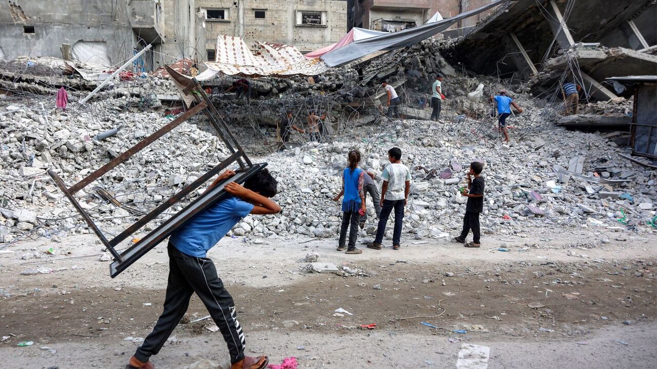 A boy walks carrying a table on his back past salvage workers scrapping the rubble of a building that was destroyed during Israel's war against Hamas in Gaza City on Aug. 16, 2026. — Photo by Omar Al-Qattaa / AFP via Getty Images
