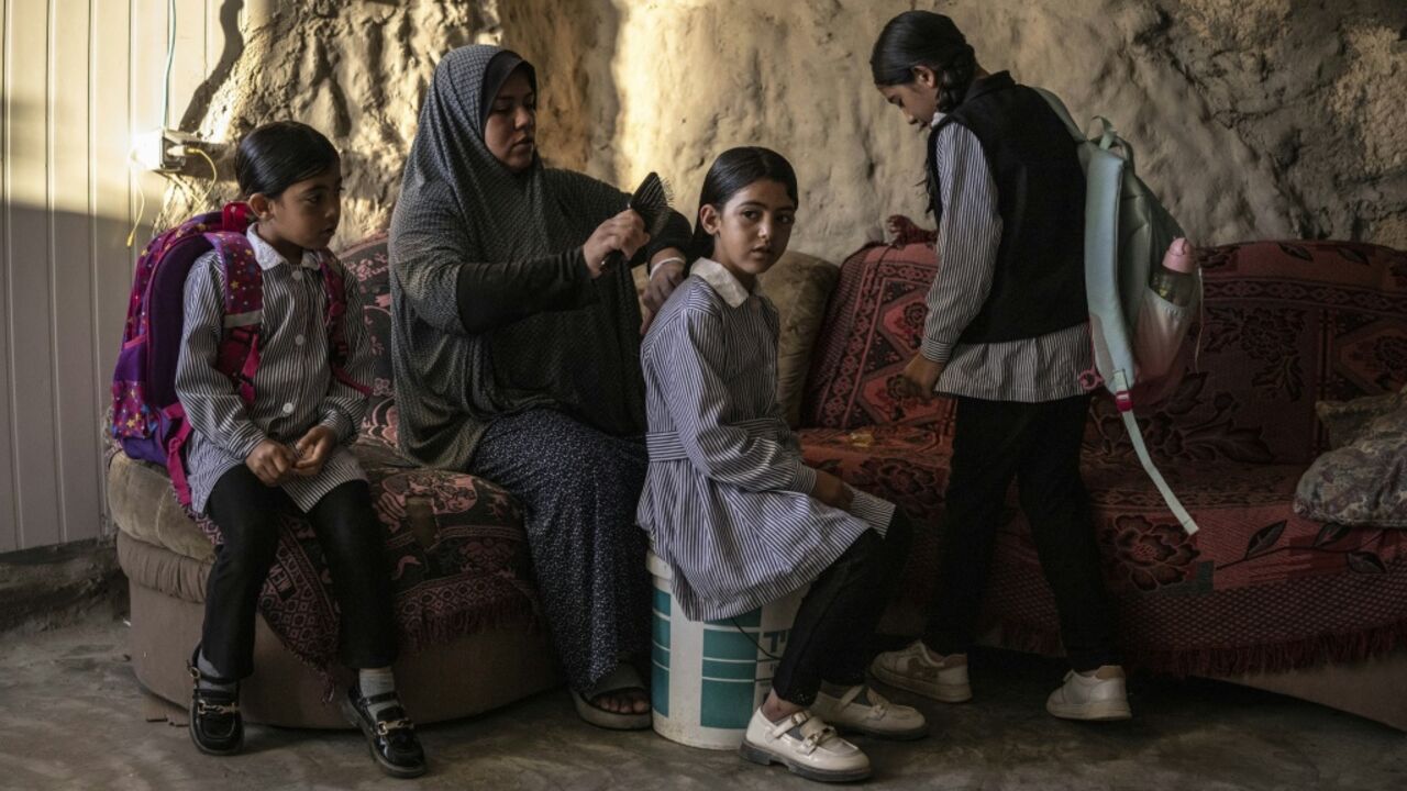 Arwa Emar brushes her daughter's hair as they prepare for school, inside a cave that the family has turned into their home