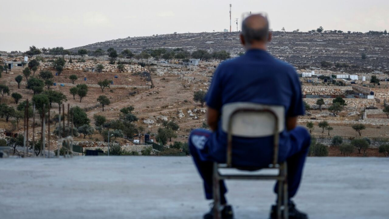 A Palestinian man sits on the rooftop of his house as he looks at a newly established Israeli settler outpost in Burqah in the Israeli-occupied West Bank