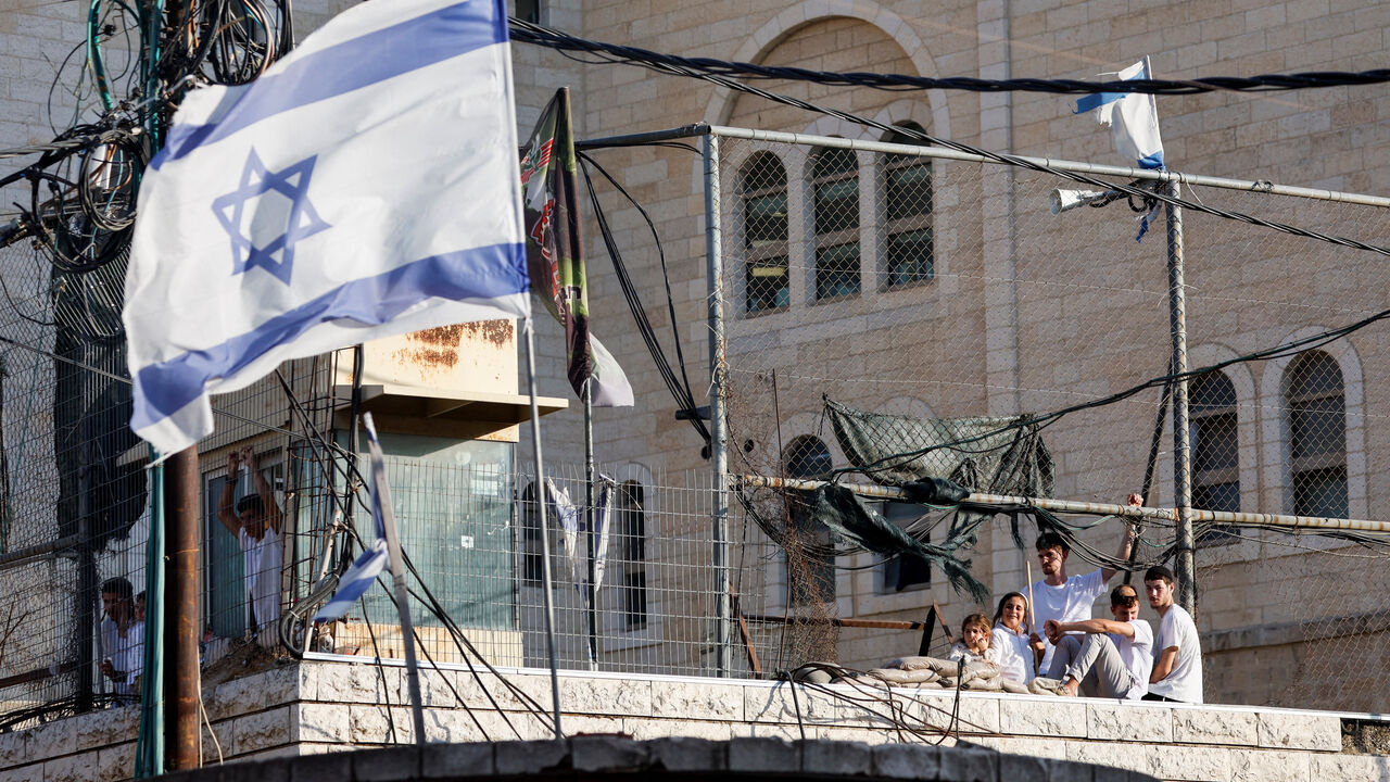 Israeli settlers look out through a metal fence, as an Israeli flag flutters nearby, on the day of their weekly tour in Hebron, in the Israeli-occupied West Bank, August 29, 2026. REUTERS/Mussa Qawasma